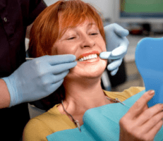 middle-aged woman smiling as she looks at her teeth in a handheld mirror