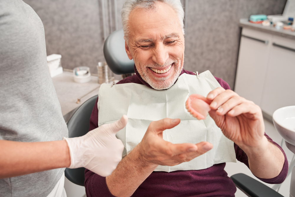 patient in dental chair holding denture